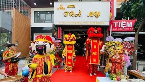 Entrada de hotel con alfombra roja, trajes tradicionales de baile del león y decoración floral.