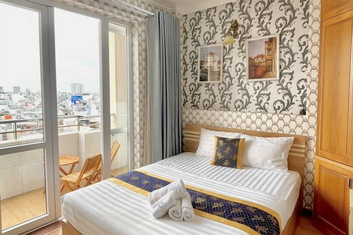 A hotel room with a large bed, a balcony with a view of the city, and a patterned wallpaper.