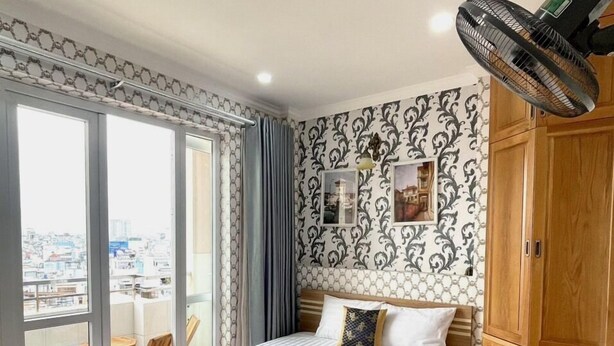 Habitación de hotel con una cama grande, piso de madera, balcón con vista a la ciudad y ventilador de techo.