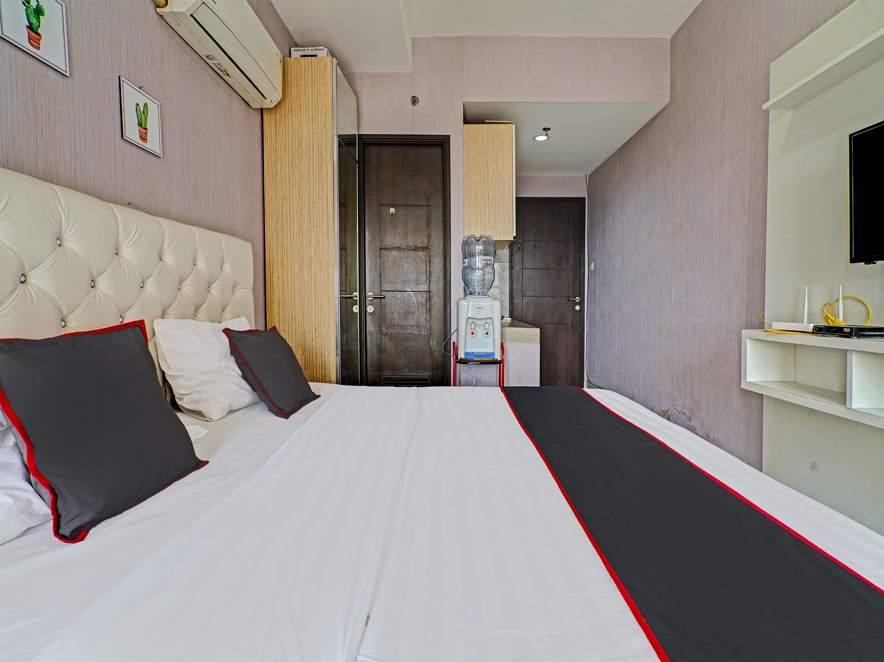 A hotel room with a large bed, a television, a water dispenser, and a bathroom visible through an open door.