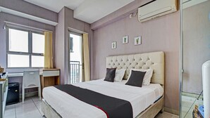 A hotel room with a large bed, a desk, and a chair. There is an air conditioning unit on the wall and a window with curtains. - OYO Life 92548 M-square Apartment By Lins Pro (Bandung)