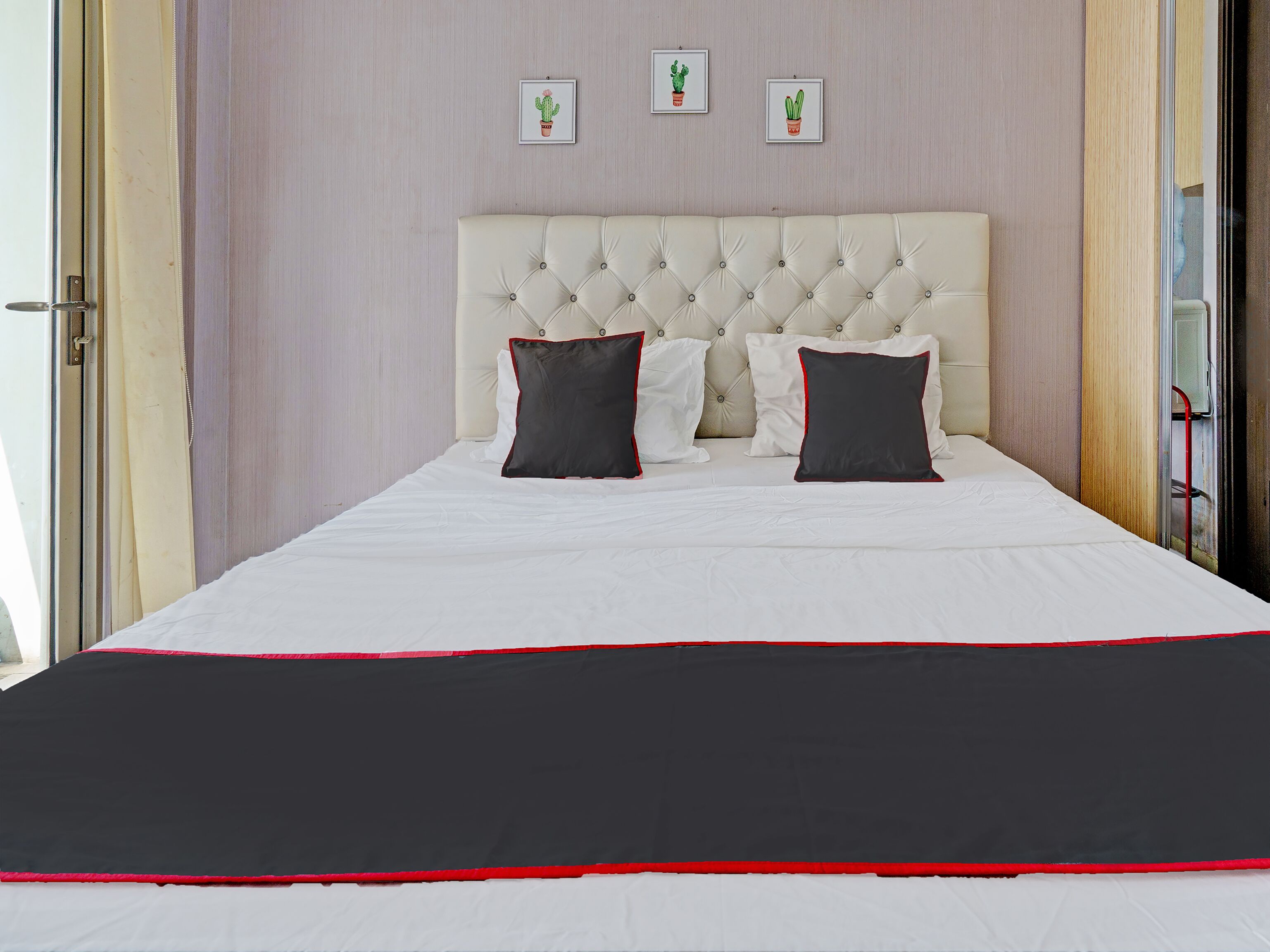 A neatly made bed with a white and red bedspread, a tufted headboard, and three framed cactus pictures on the wall.