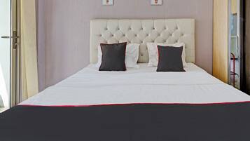 A neatly made bed with a white and red bedspread, a tufted headboard, and three framed cactus pictures on the wall.