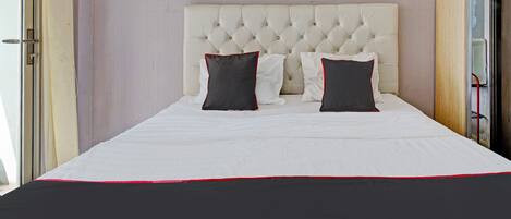 Un letto rifatto con cura, con una coperta bianca e rossa, una testiera imbottita e tre quadri raffiguranti cactus appesi al muro.