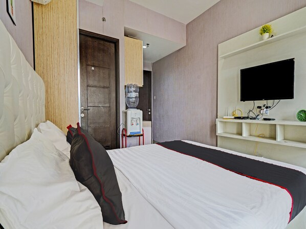 Habitación de hotel con cama, dispensador de agua, televisión y estante con un reloj.