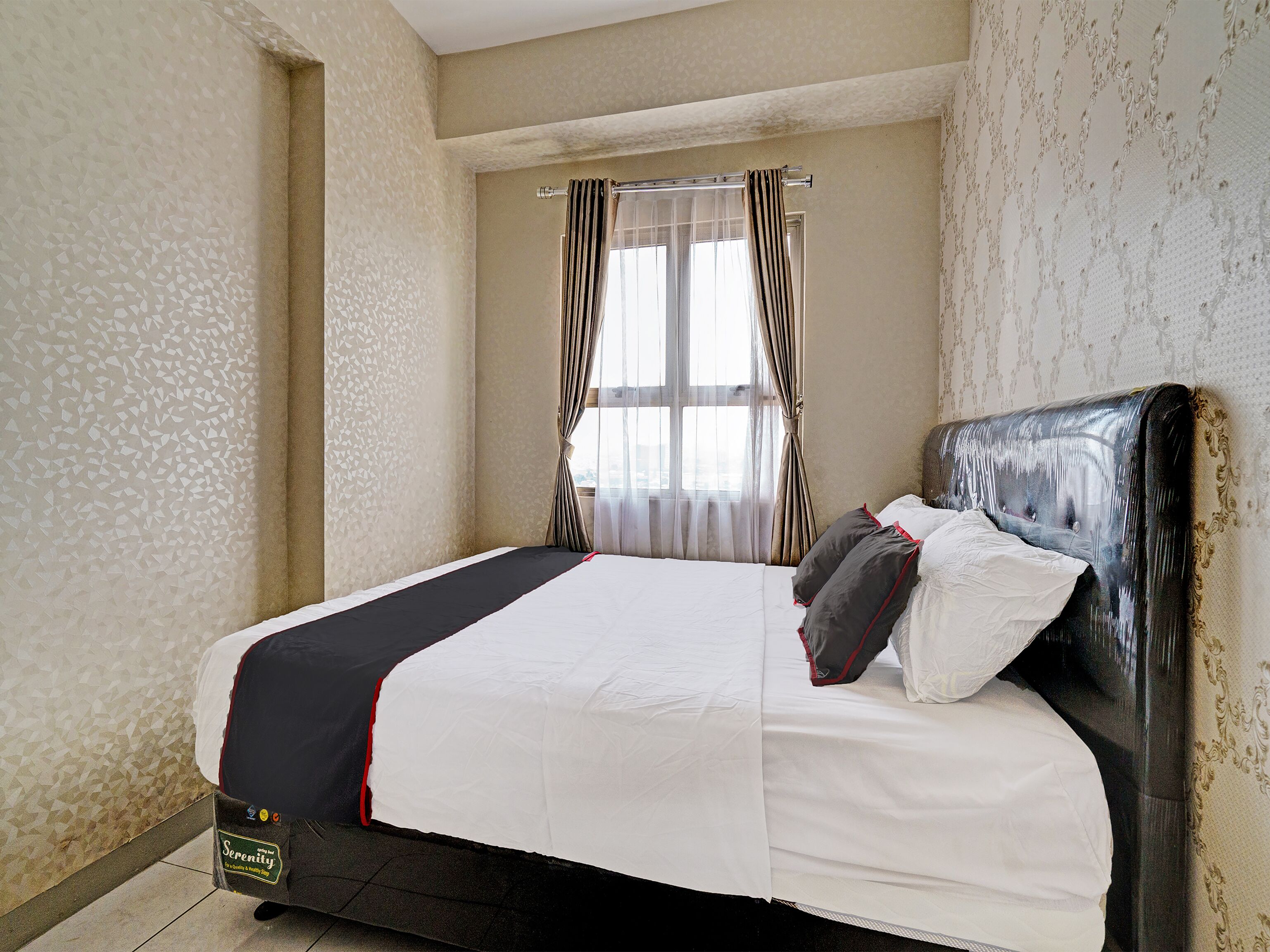 A neatly made bed with a black and white bedspread, a headboard with a glossy finish, and a window with sheer curtains.