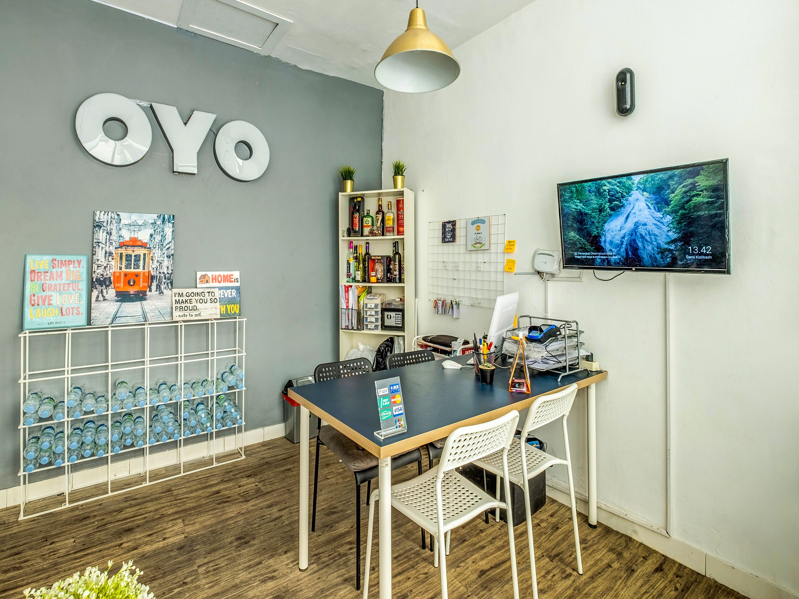 A modern office space with a large 'OYO' sign, a wooden table with chairs, a TV on the wall, and a shelf with various items.