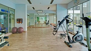 A spacious gym with various exercise equipment, large windows, and a mirrored wall. - OYO Life 92548 M-square Apartment By Lins Pro (Bandung)