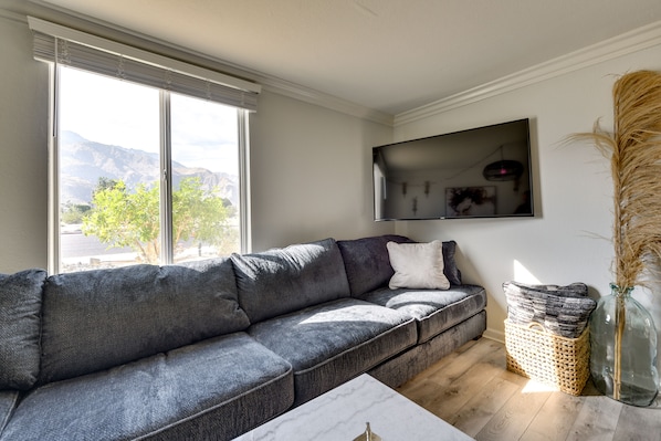 Relax in this stylish living room with a large sofa, flat-screen TV, and a beautiful view of the surrounding greenery and mountains.