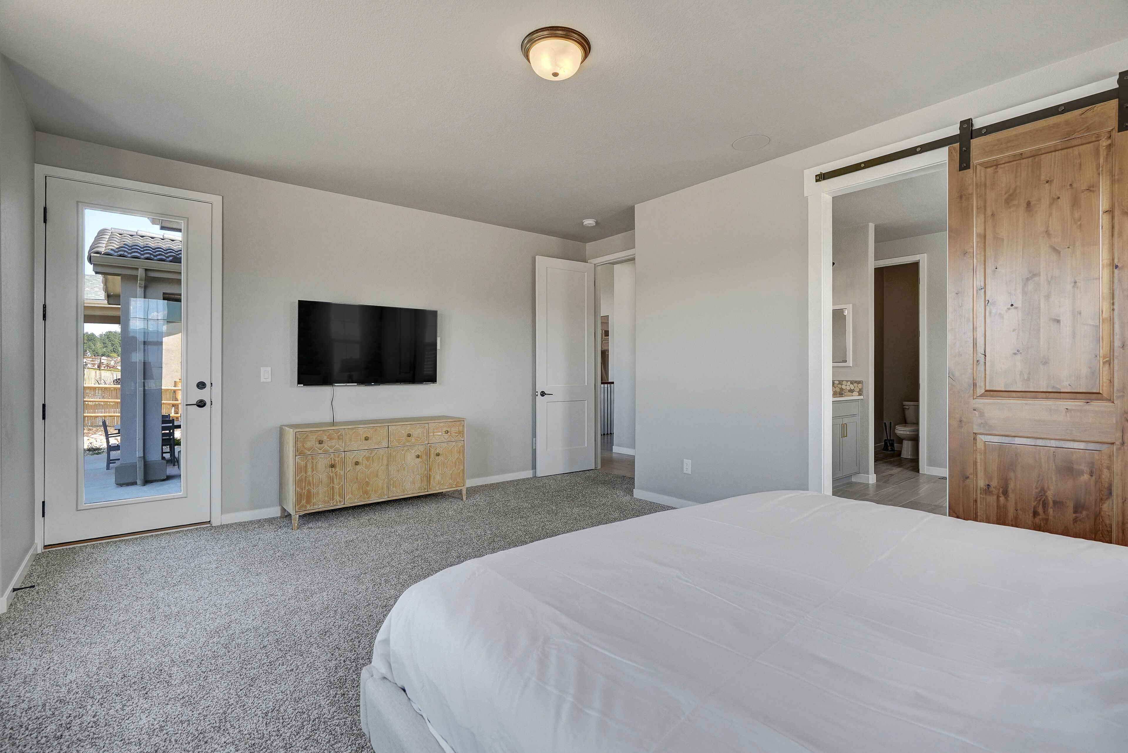 Ein Schlafzimmer mit einem großen Bett, einem an der Wand montierten Fernseher, einem Holzschrank und einer Schiebetür zum Badezimmer.