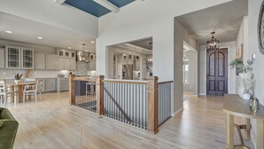 A spacious kitchen with white cabinets, a dining area with a wooden table and chairs, and a staircase with a wooden railing.