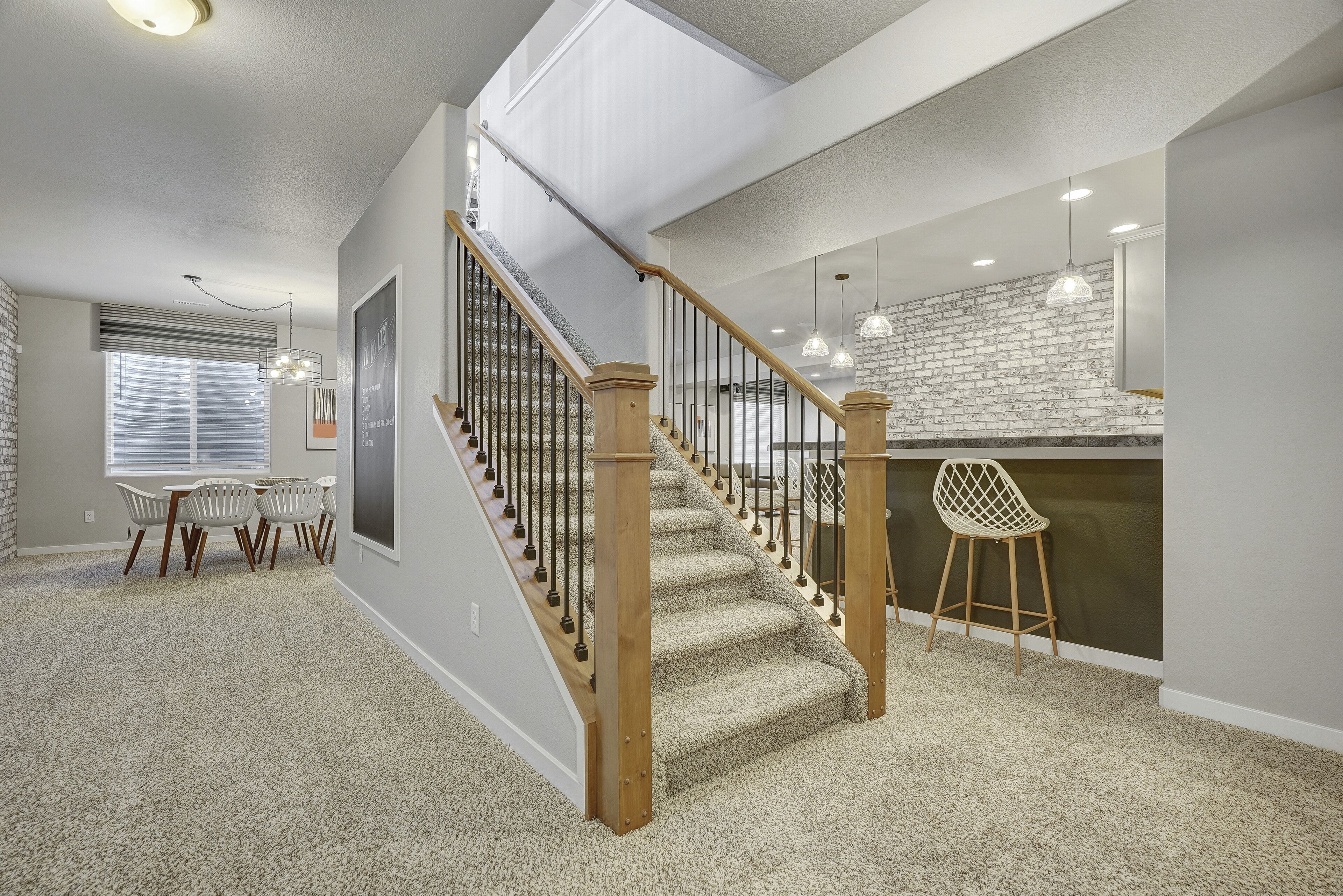 A spacious living area with a staircase, a dining area with a table and chairs, and a kitchen with pendant lighting.