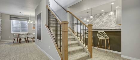A spacious living area with a staircase, a dining area with a table and chairs, and a kitchen with pendant lighting.