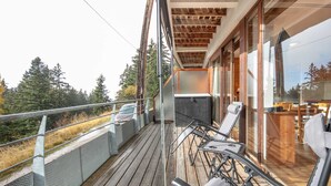 Une terrasse en bois avec une rambarde, une voiture garée sur le côté et une vue sur les arbres et les montagnes.