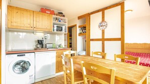 Une cuisine compacte dotée de meubles en bois, d’un lave-linge, d’un four à micro-ondes et d’un coin repas avec une table et des chaises en bois.