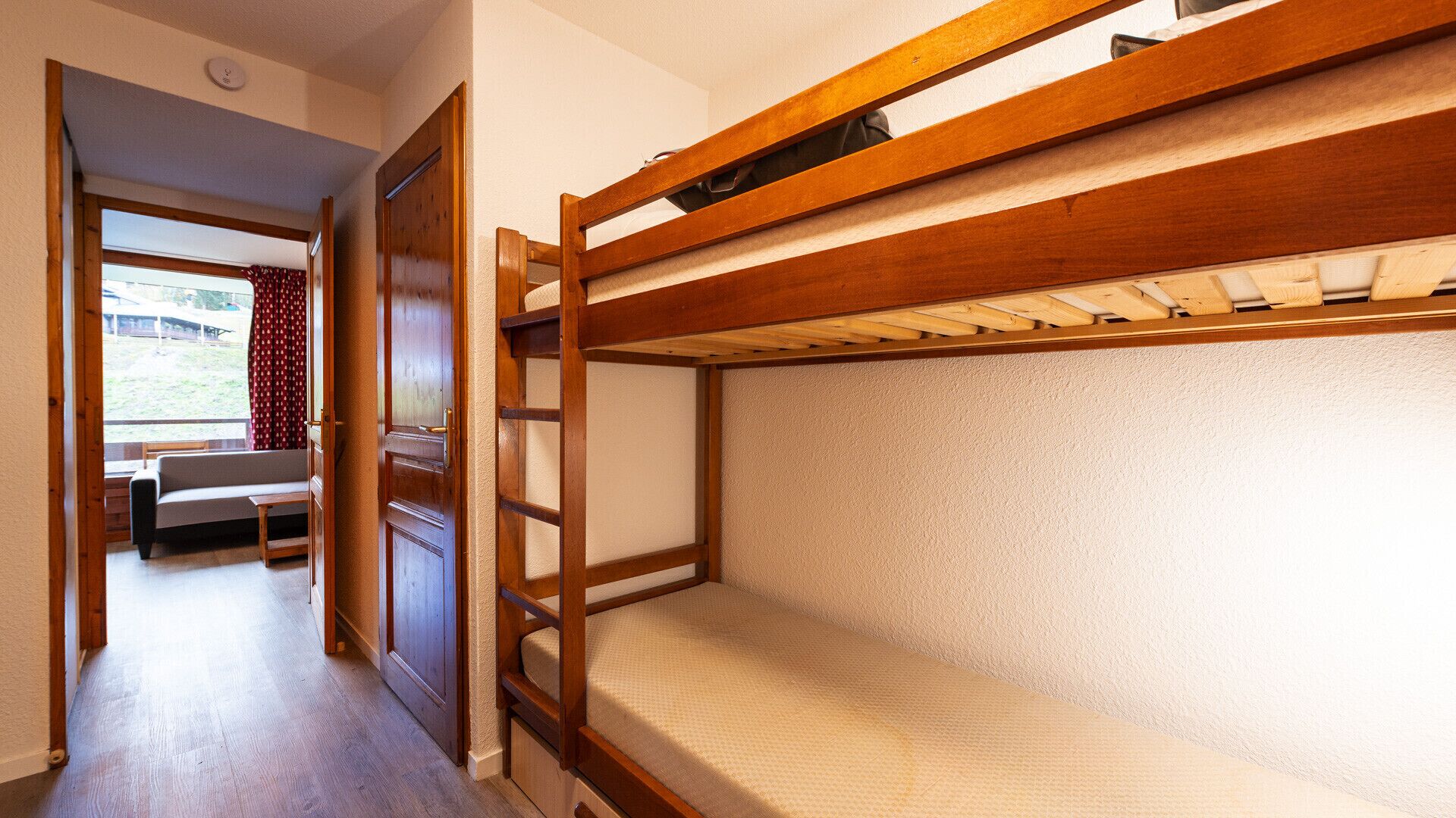 A bunk bed room with a wooden ladder, a sofa, and a window with curtains.