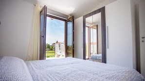 Une chambre avec un lit, un grand miroir et une porte coulissante ouverte donnant sur un espace extérieur aménagé avec des chaises.