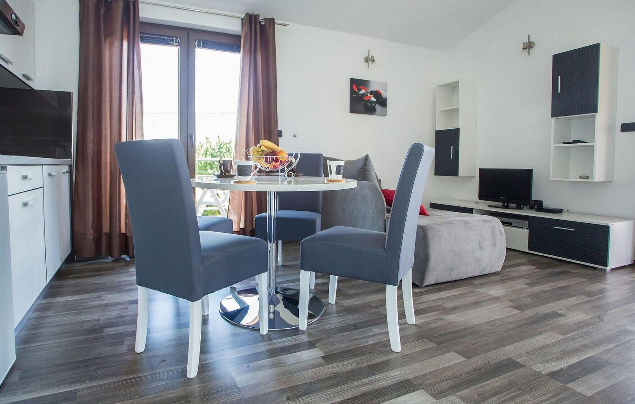 A modern living room with a round dining table, two blue chairs, a grey sofa, a TV, and a cabinet.