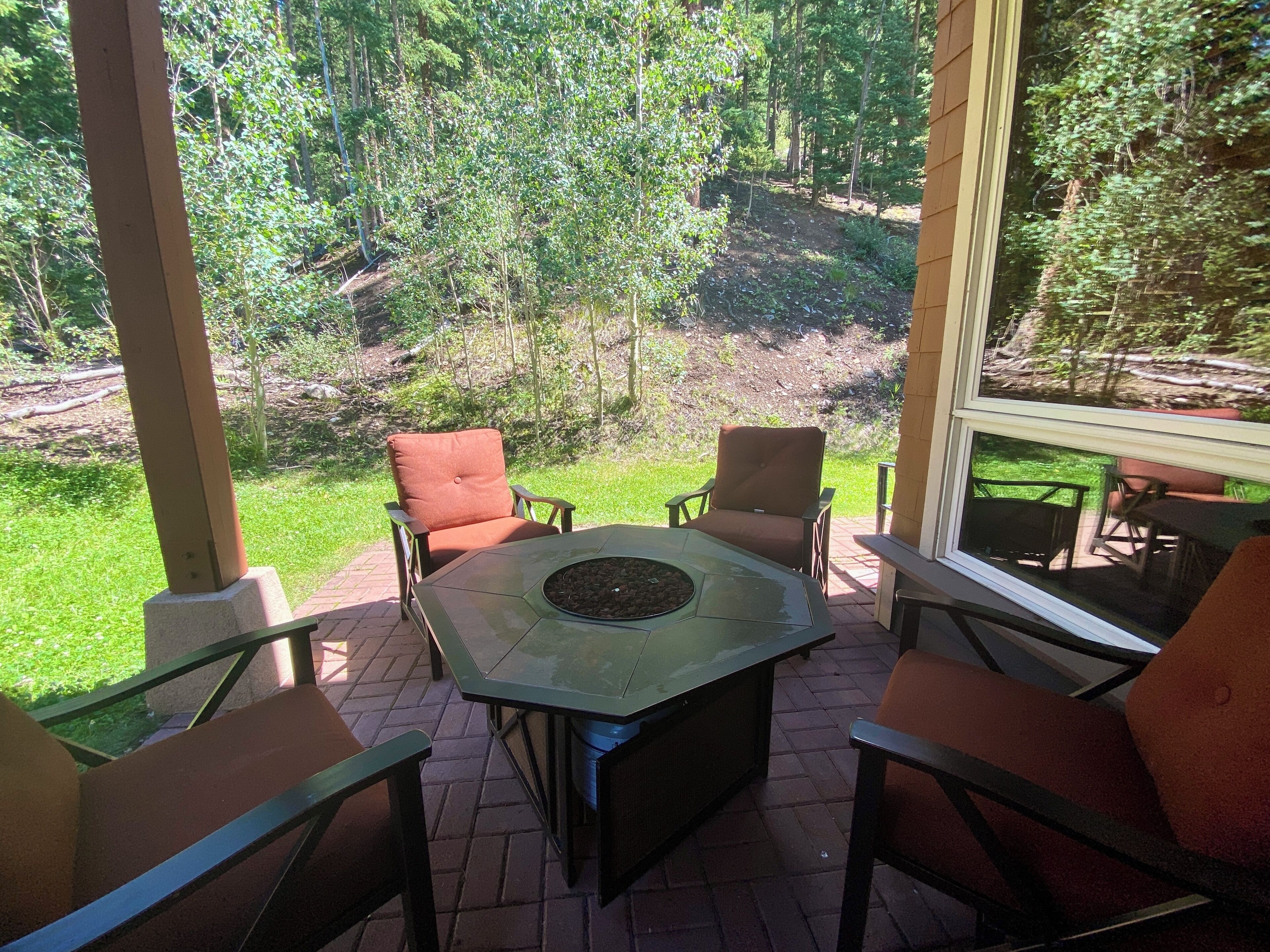 A covered patio with a hexagonal table and four chairs, overlooking a wooded area.