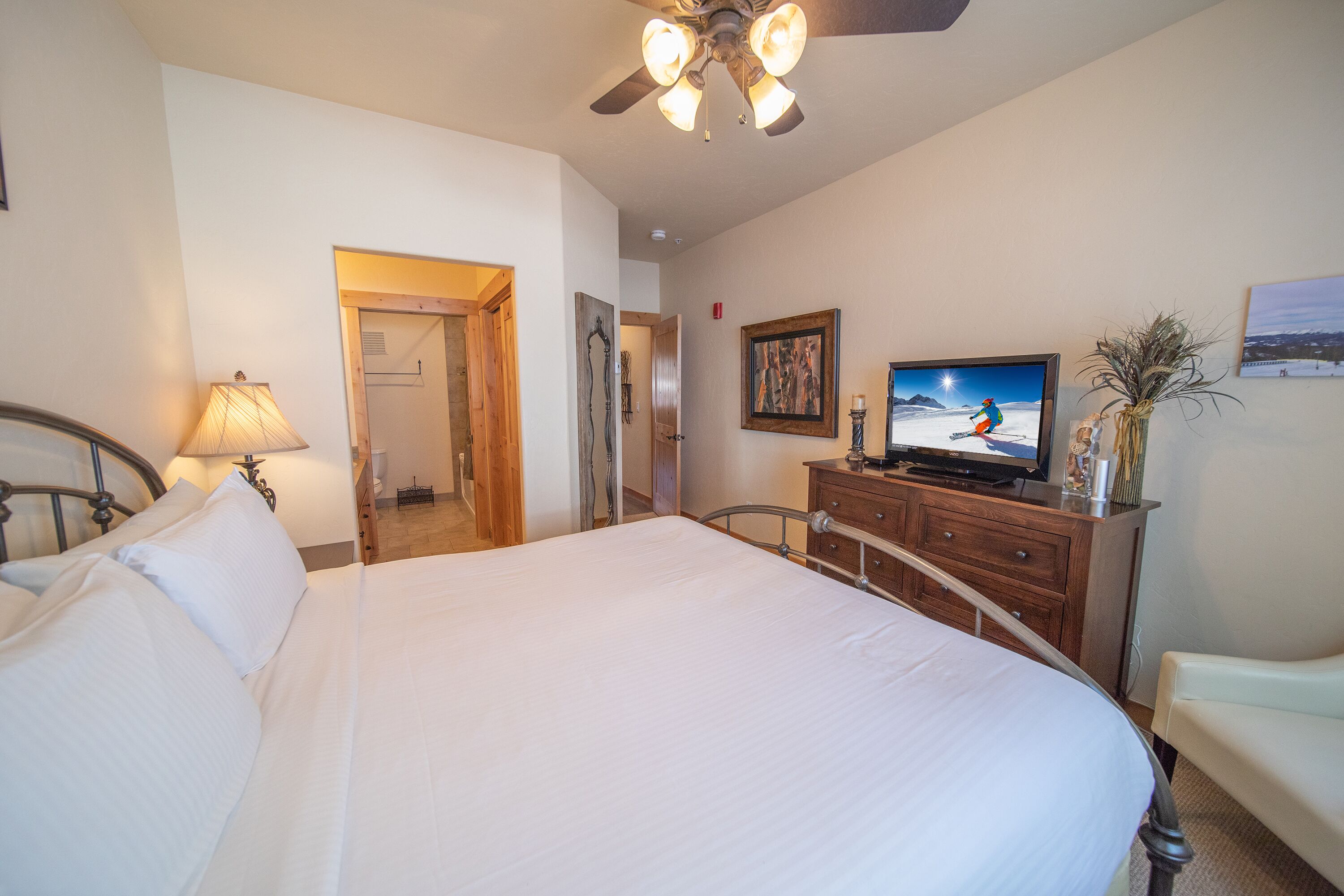Un dormitorio con una cama grande, televisión, cómoda y una silla.