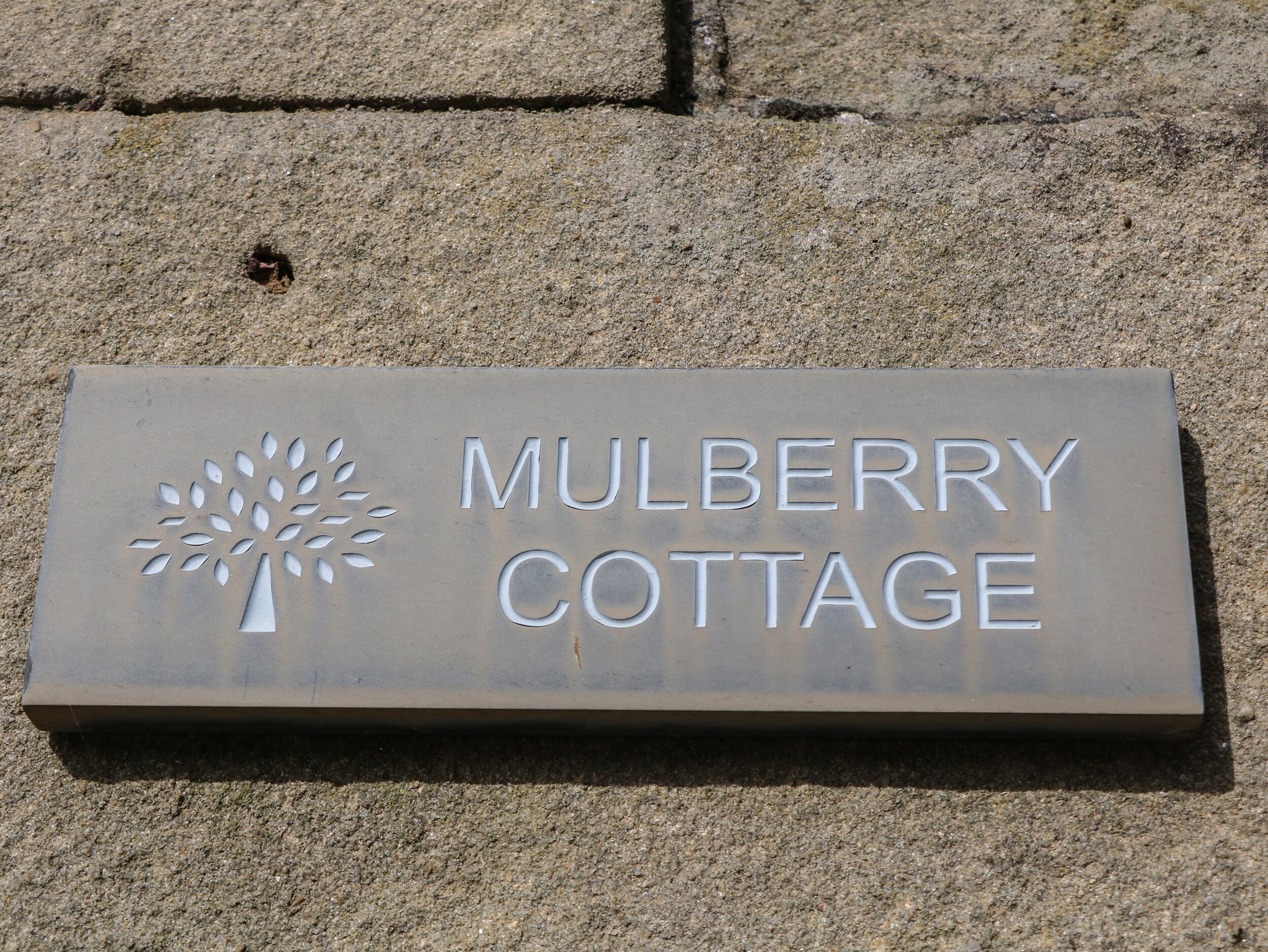 A metal sign with the text "MULBERRY COTTAGE" and a tree design.