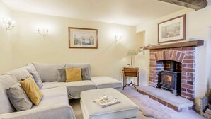 Una sala de estar acogedora con sofá, reposapiés, chimenea y cuadros en la pared.