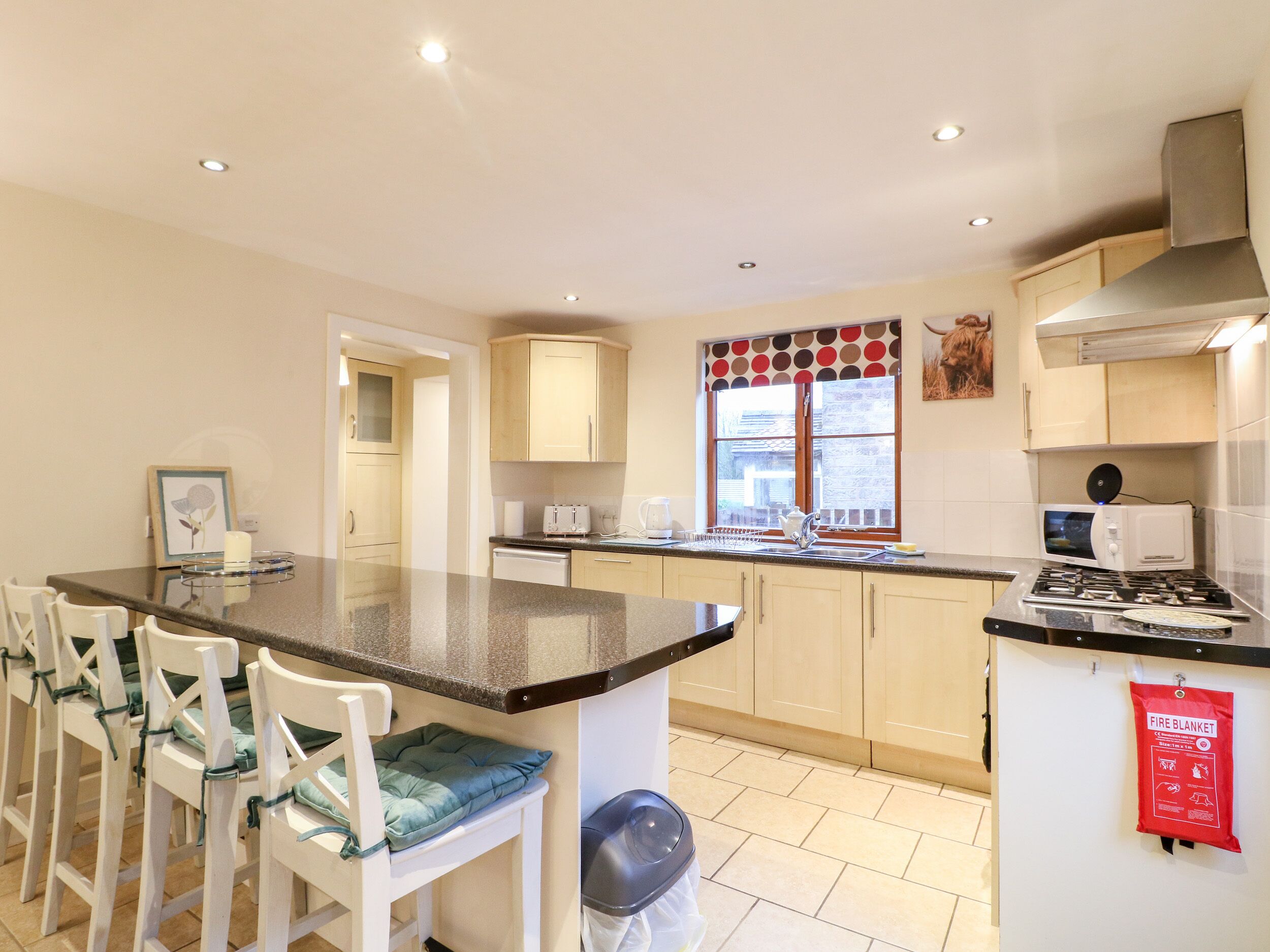 A modern kitchen with a central island, white chairs, and a fire blanket on the wall.