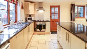 Une cuisine équipée d’une cuisinière, d’un four à micro-ondes et d’un évier. Il y a une fenêtre avec des rideaux et une porte avec des panneaux de verre.