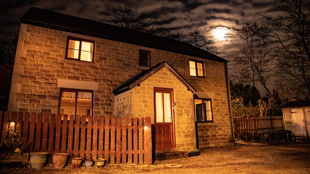 Une maison en pierre avec une porte et des fenêtres en bois, entourée d’une clôture en bois et agrémentée de plantes en pot.