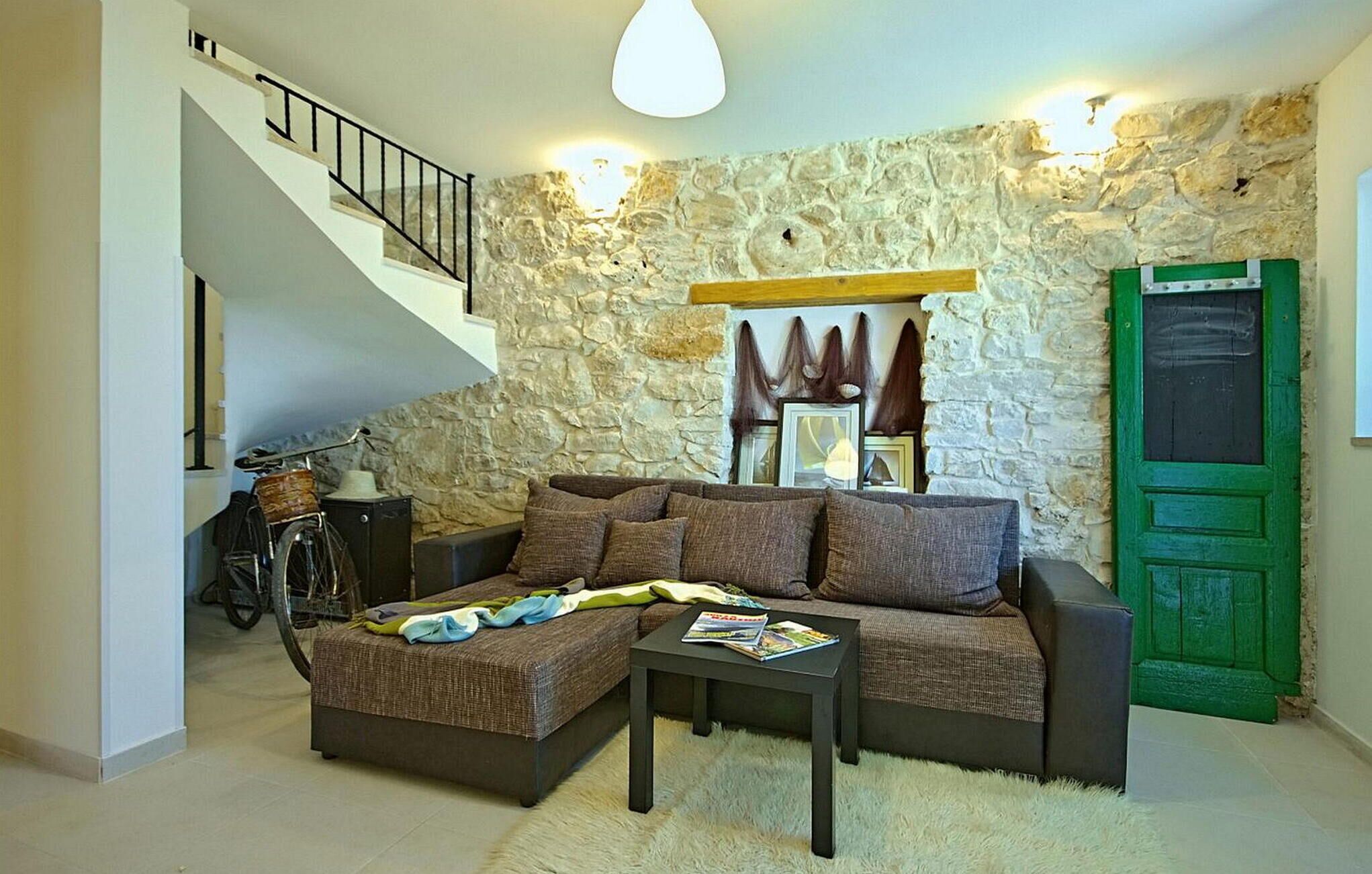Uma sala de estar com parede de pedra, porta verde, escada e uma bicicleta.