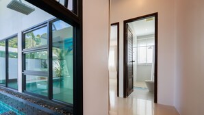 A modern hotel room with a large window overlooking a pool, a bathroom with a toilet and sink, and a clean, tiled floor. - Paradise Found (Rawai)