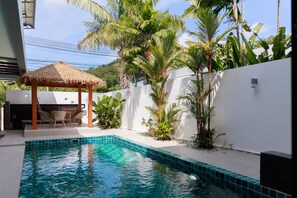 A swimming pool with a thatched gazebo, surrounded by tropical plants and a white wall. - Paradise Found (Rawai)