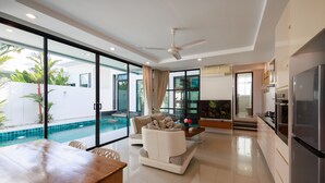 A modern living room with a pool view, a dining area, and a kitchen. - Paradise Found (Rawai)