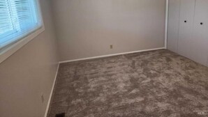 A room with beige walls, a carpeted floor, a window with blinds, and a closet with two doors. - Cozy country house near major stores, markets. Ideal for your perfect vacation. (Nampa)