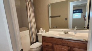 A bathroom with a toilet, a shower, a sink, and wooden cabinets. - Cozy country house near major stores, markets. Ideal for your perfect vacation. (Nampa)