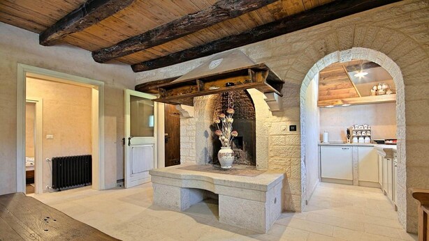 Un intérieur rustique avec une cheminée en pierre, un banc en bois et un coin cuisine doté de placards.