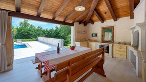 Une cuisine spacieuse avec un grand îlot central, un coin repas avec un banc en bois et une vue sur une piscine.