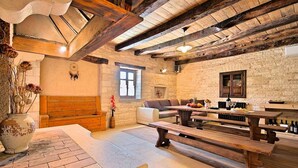Un intérieur rustique avec des poutres apparentes, un mur en pierre, un banc en bois, un canapé et une table sur laquelle se trouvent une bouteille et des verres.