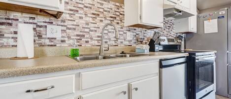 Una cocina con armarios blancos, un lavamanos de acero inoxidable, lavavajillas y refrigerador.
