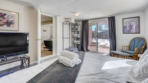 A modern hotel room with a large bed, a flat-screen TV, a seating area with a chair, a small table, and a balcony with a view. - Always Somerset (Colorado Springs)