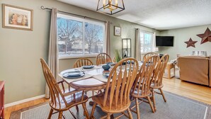 A dining area with a round table, wooden chairs, and a chandelier. There is a television and a cabinet in the background. - Always Somerset (Colorado Springs)