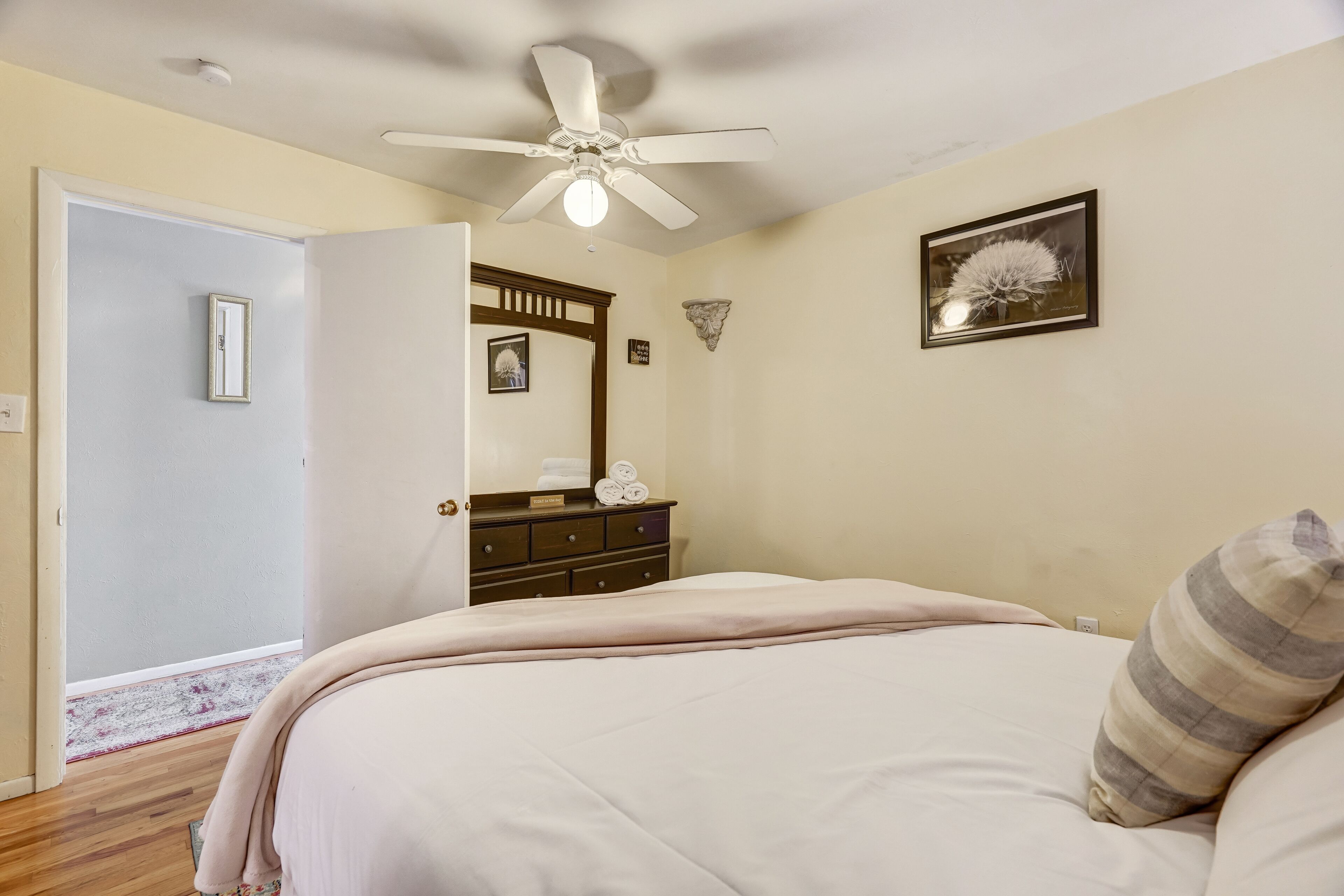 Een slaapkamer met een bed, een plafondventilator, een dressoir, een spiegel en een ingelijst schilderij aan de muur.