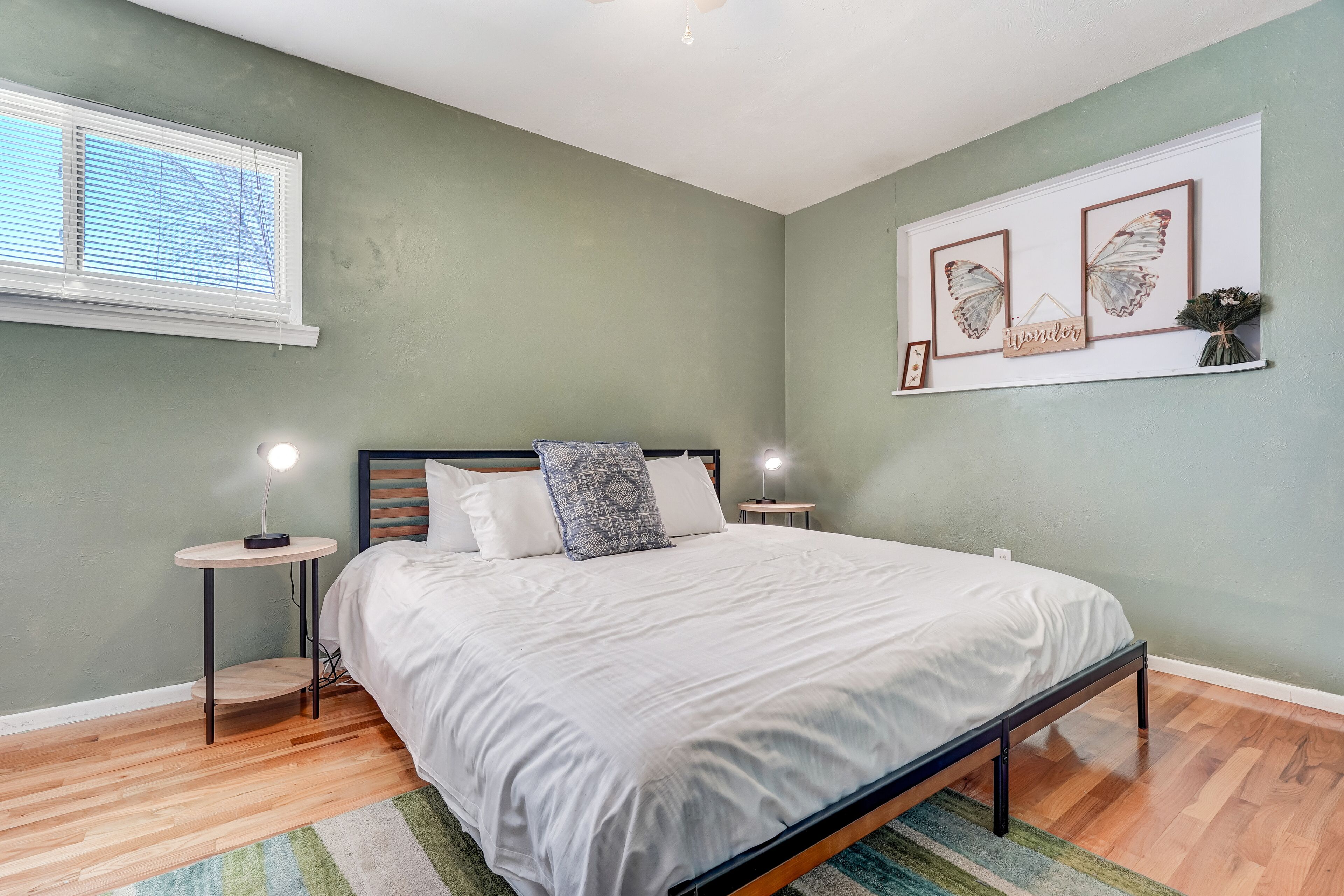 A bedroom with a bed, two bedside tables, a window, and wall art.