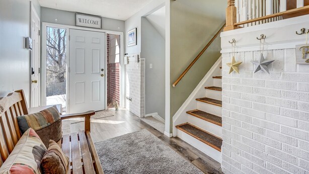 A home interior with a staircase, a bench, and a 'WELCOME' sign. - Always Somerset (Colorado Springs)
