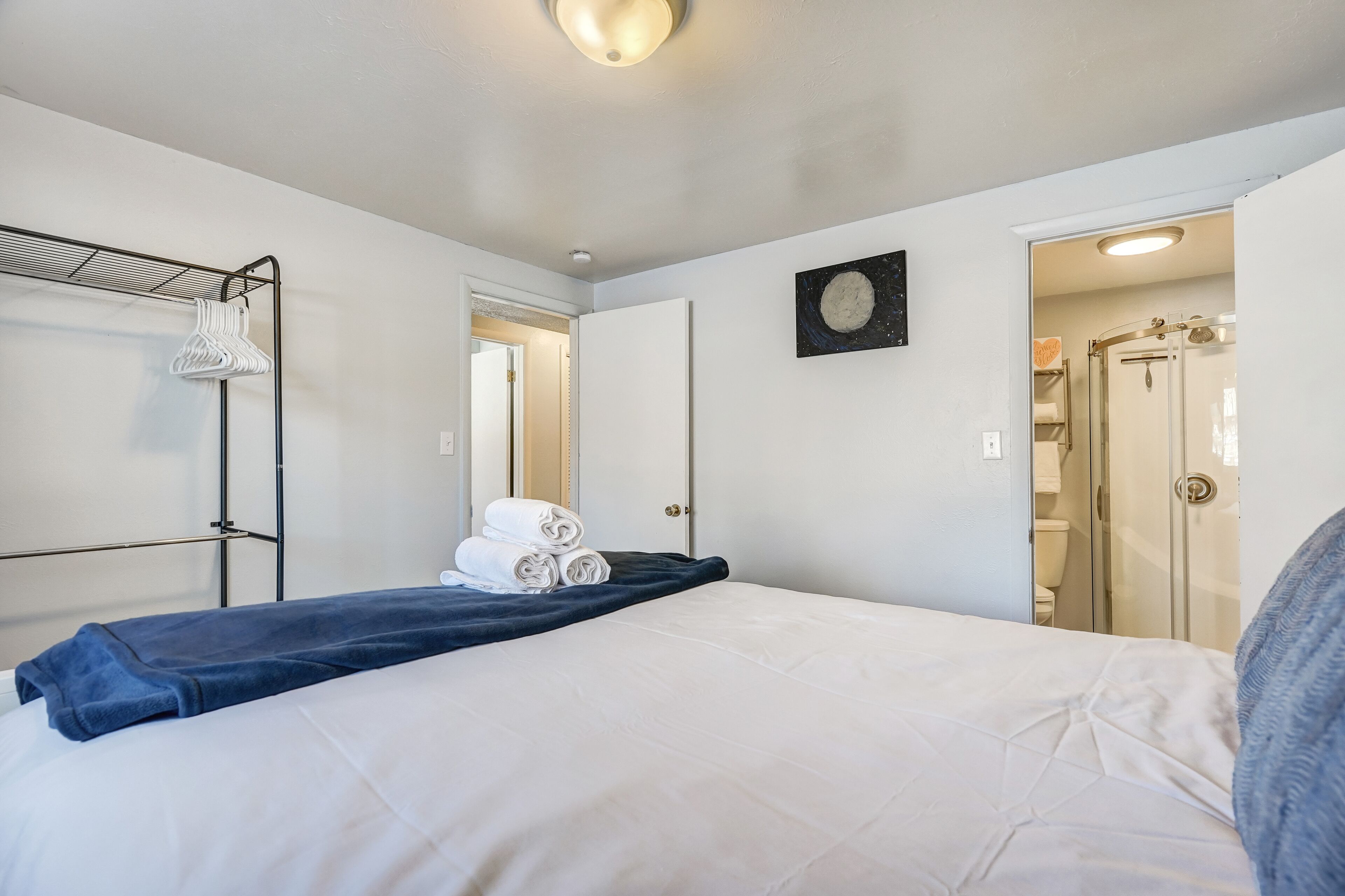 Une chambre d’hôtel comprenant un lit, un porte-serviettes, une porte donnant accès à une salle de bain et une œuvre d’art accrochée au mur.