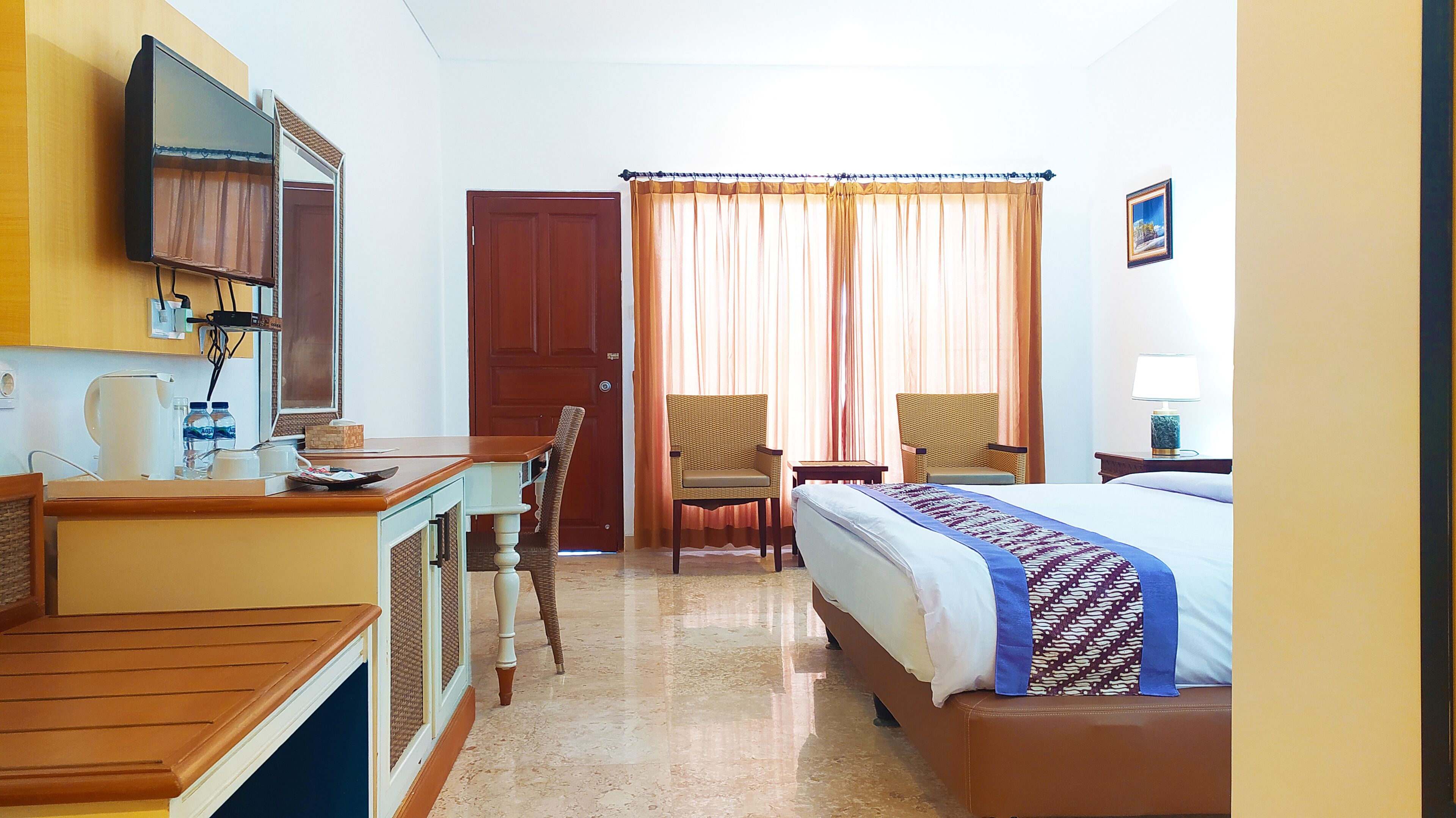 A hotel room with a bed, a desk, a chair, a television, and a window with curtains.
