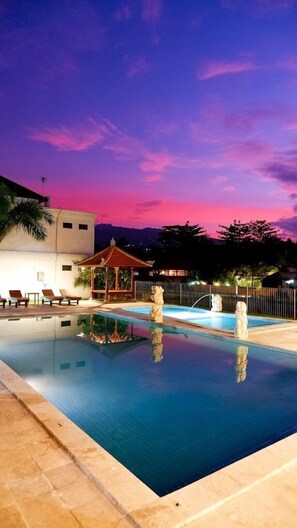 A swimming pool with a gazebo and lounge chairs, surrounded by a fence and palm trees. - Puri Lovina (Banjar)