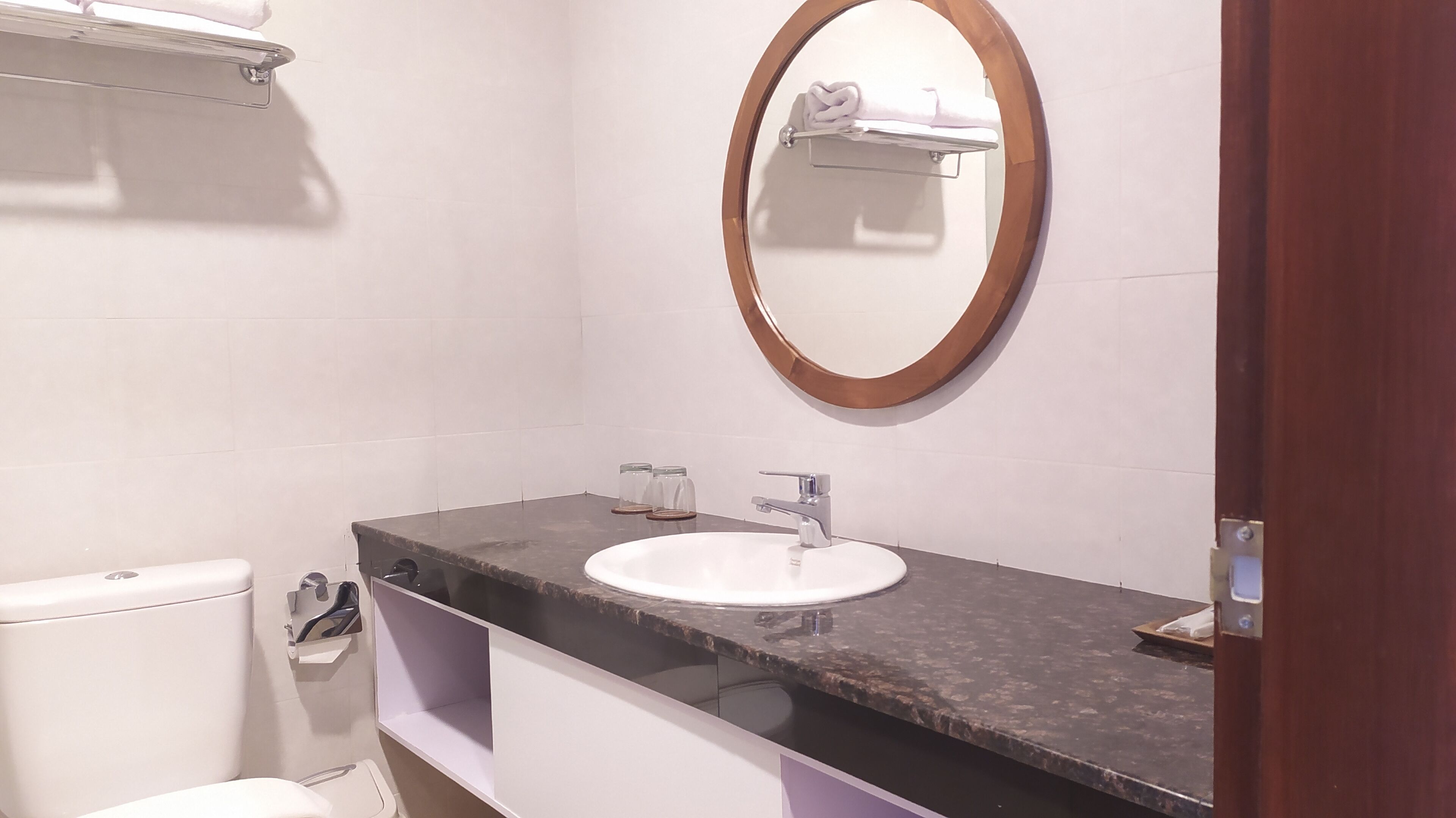 A bathroom with a white sink, a round mirror, and a toilet.