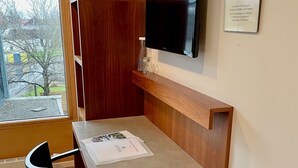 Una camera compatta con una scrivania in legno, una sedia, una TV a schermo piatto montata a parete e una finestra con tende.