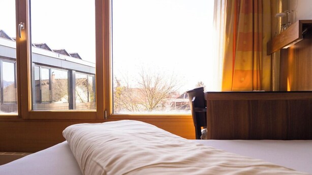 Una camera da letto con un'ampia finestra, un letto con biancheria bianca e un comodino in legno.